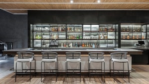 Un espace bar avec un plafond en bois, un long comptoir doté de plusieurs étagères à bouteilles et trois tabourets de bar.