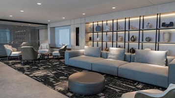 A modern living room with a grey sofa, ottoman, and chairs, a patterned rug, and a wall with shelves displaying various decorative items.