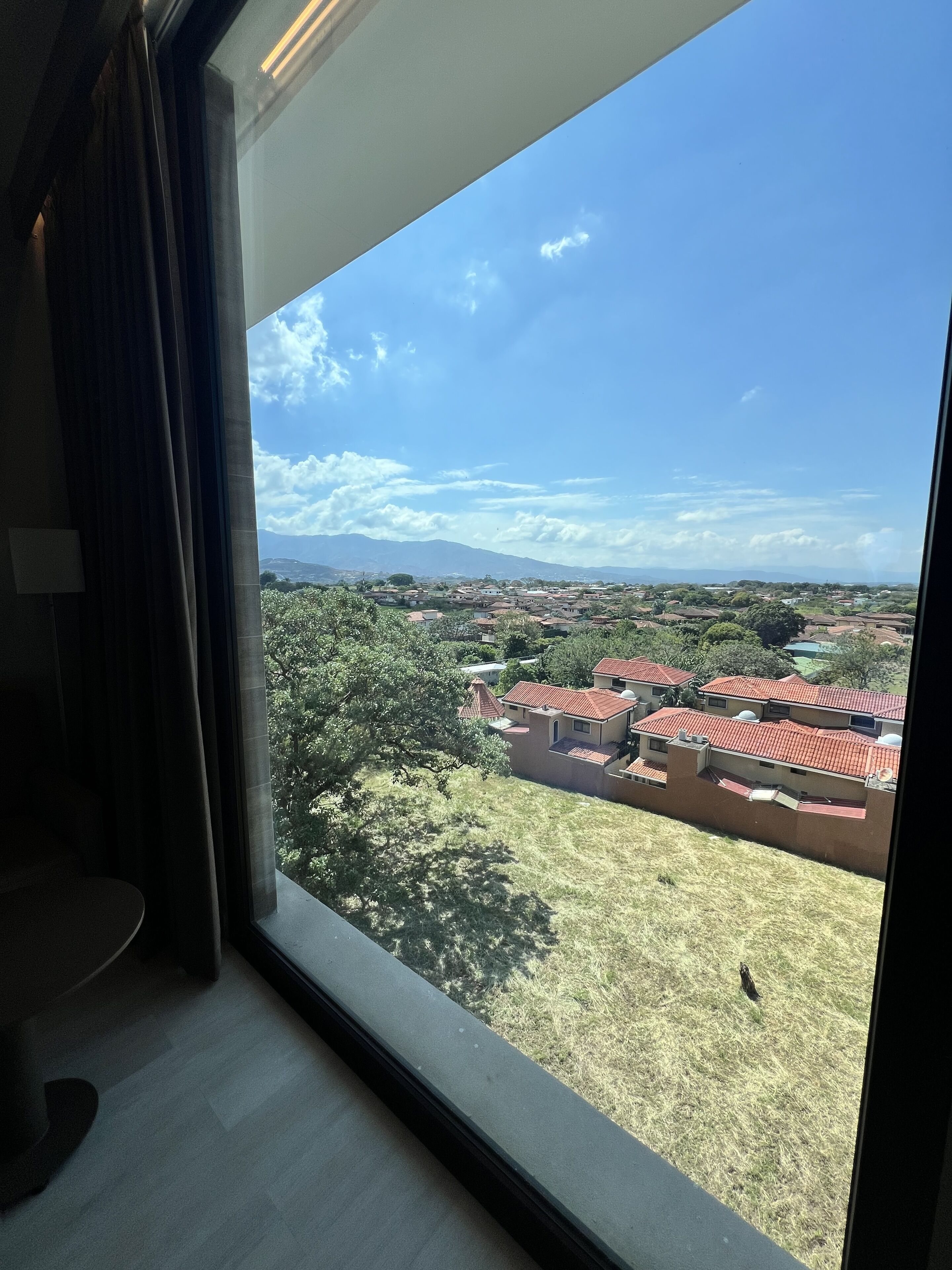 Habitación con un amplio ventanal que da a una zona residencial con casas y árboles.