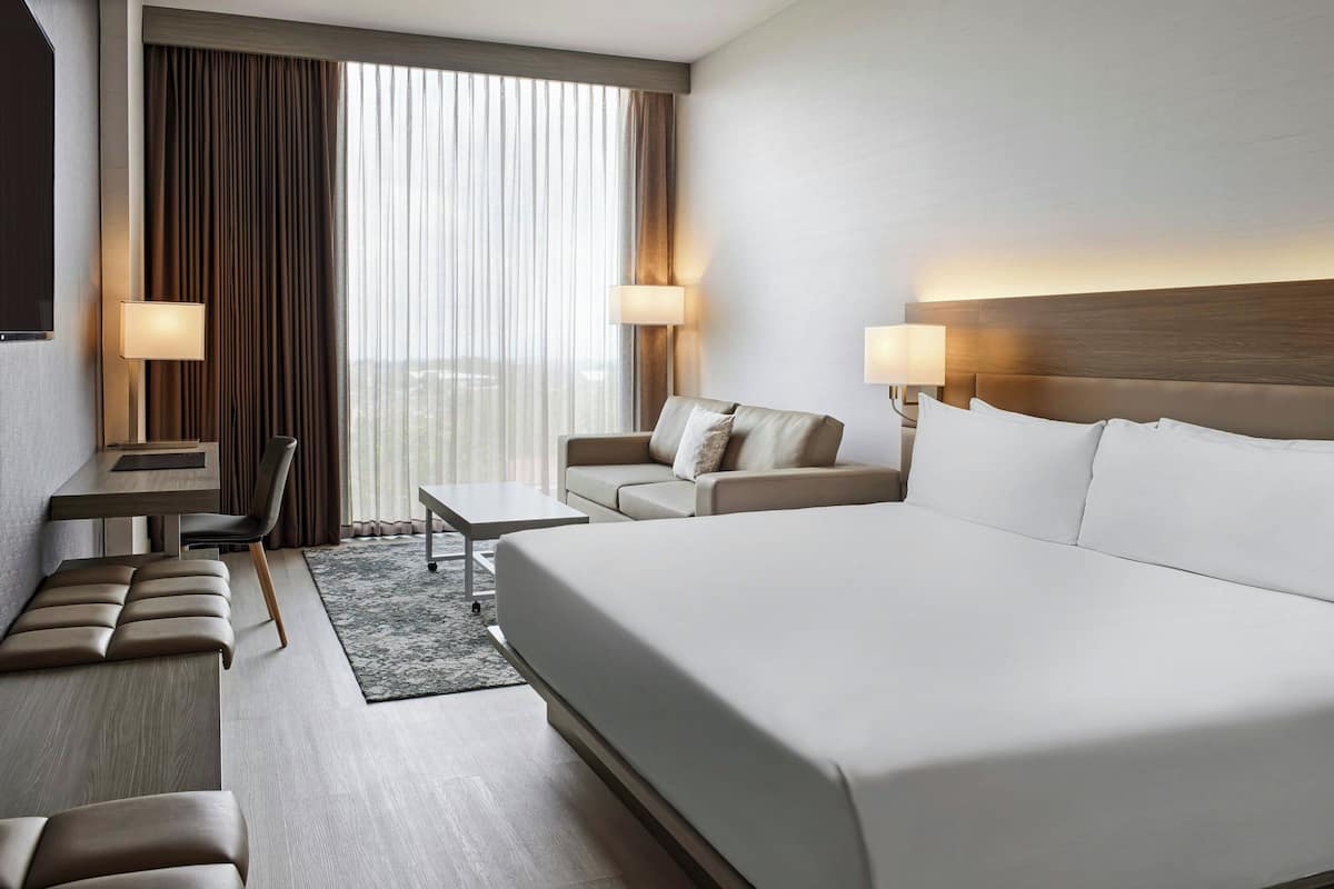 Een hotelkamer met een groot bed, een bank, een bureau en een stoel. Aan weerszijden van het bed staan twee lampen.