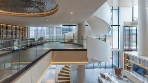 Un hall d’hôtel spacieux et moderne, doté d’un escalier à la forme incurvée, d’une rambarde en verre et d’un espace salon avec des canapés et une table basse.