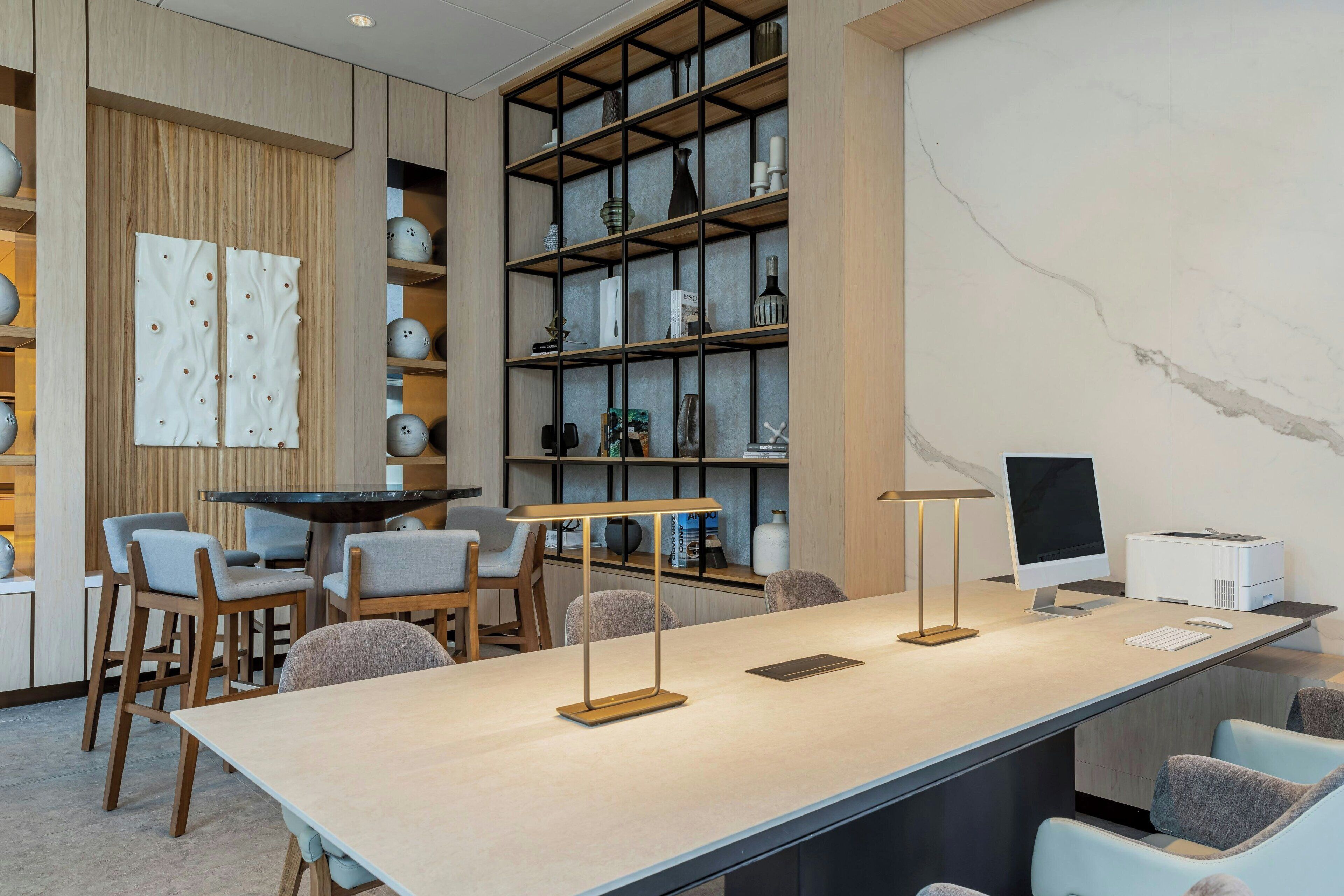 Un espace de bureau moderne comprenant une grande table, des chaises, un ordinateur et des étagères remplies de divers objets.