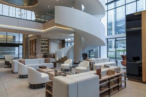 Un hall d’entrée spacieux, doté d’un escalier central en colimaçon, de meubles modernes et de grandes fenêtres offrant une vue sur l’extérieur.