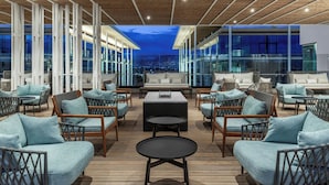 Un salon sur le toit, aménagé avec des meubles en osier, une table centrale et offrant une vue sur la ville au crépuscule.