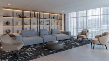 Ein modernes Wohnzimmer mit einem grauen Sofa, zwei Sesseln, einem Couchtisch und einer Wand mit Regalen, auf denen verschiedene dekorative Gegenstände präsentiert werden.