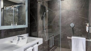 Un baño moderno con ducha de vidrio, lavamanos blanco y espejo grande.