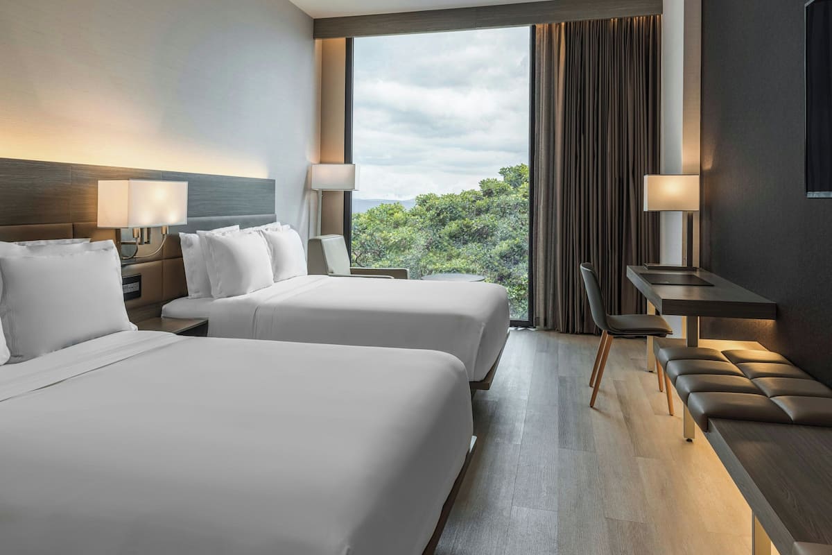 Een hotelkamer met twee bedden, een bureau en uitzicht op de omgeving.
