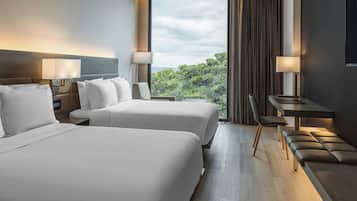 A hotel room with two beds, a desk, and a view of the outdoors.
