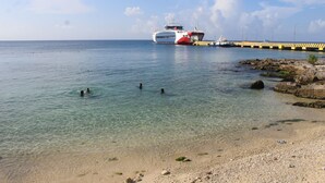 A beach with clear water, a pier, and a large boat.