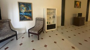 A room with two patterned chairs, a white cabinet with drawers, a painting on the wall, and a tiled floor.