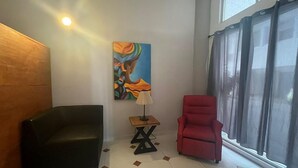 A room with a black sofa, a red chair, a small table with a lamp, and a painting on the wall.