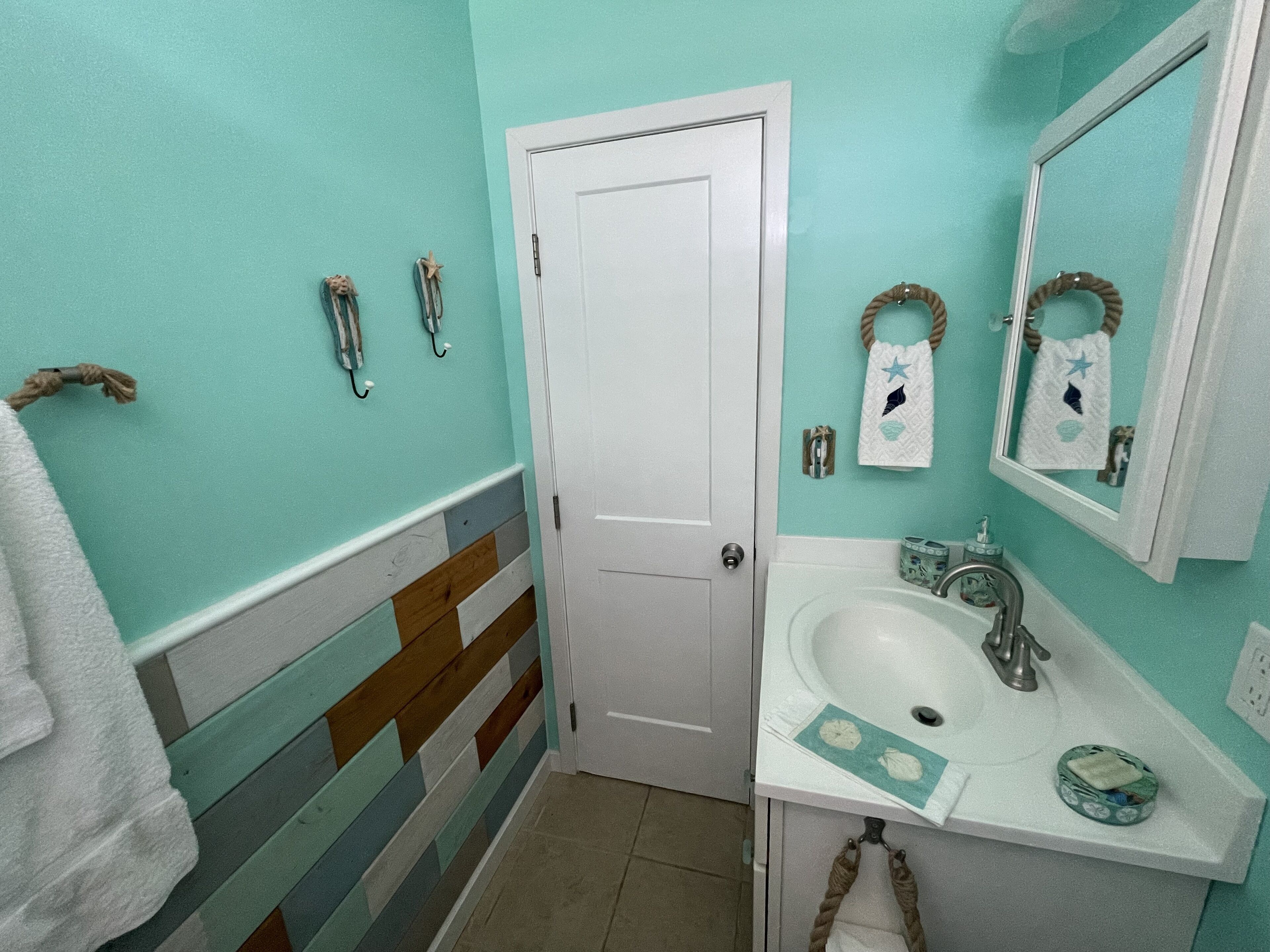 Une salle de bain avec un mur à rayures, une porte blanche, un lavabo avec un miroir et des serviettes décoratives.