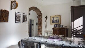 Un coin repas avec une table recouverte d’une nappe à motifs, une horloge au mur et des tableaux encadrés.