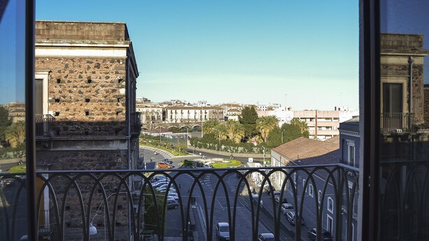 Une vue depuis un balcon donnant sur une rue de la ville, avec des bâtiments historiques et un ciel bleu dégagé.