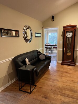 A living room with a black leather sofa, a side table, a wall-mounted mirror, and a grandfather clock.