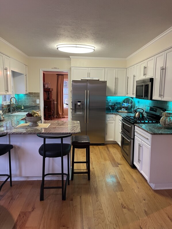 A modern kitchen with white cabinets, a stainless steel refrigerator, a microwave, a stove, and a granite countertop.