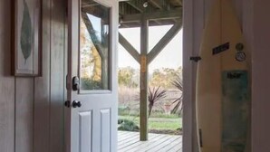 Une pièce avec un plancher en bois, une porte blanche dotée d’un panneau de verre et une planche de surf appuyée contre le mur.