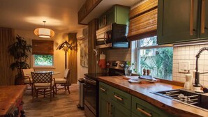 Une cuisine avec des meubles de couleur verte, un plan de travail en bois et une fenêtre donnant sur un paysage verdoyant.
