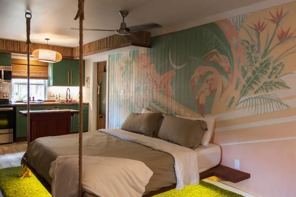 A bedroom with a large bed, a ceiling fan, and a mural on the wall.