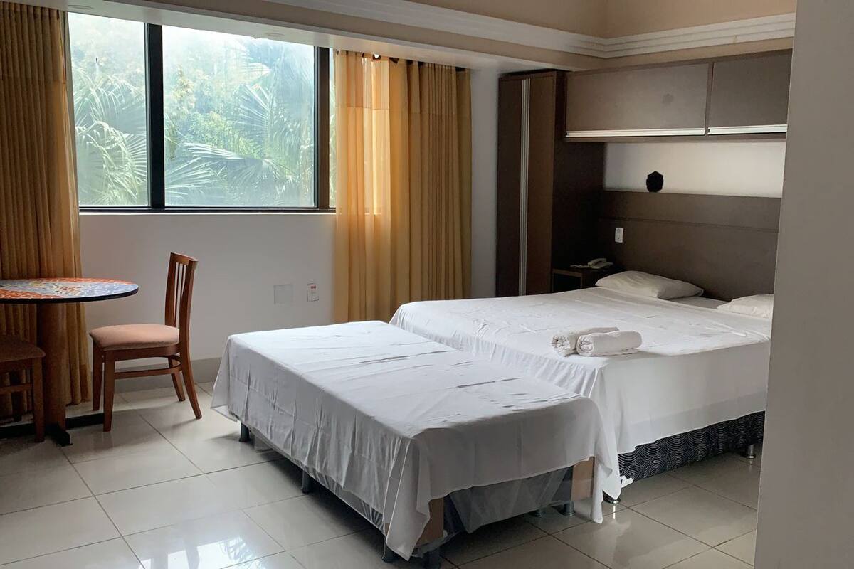 A hotel room with two beds, a small table with a chair, and a window with curtains.