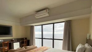 Habitación de hotel con una cama grande, un escritorio, un televisor y vista al mar.