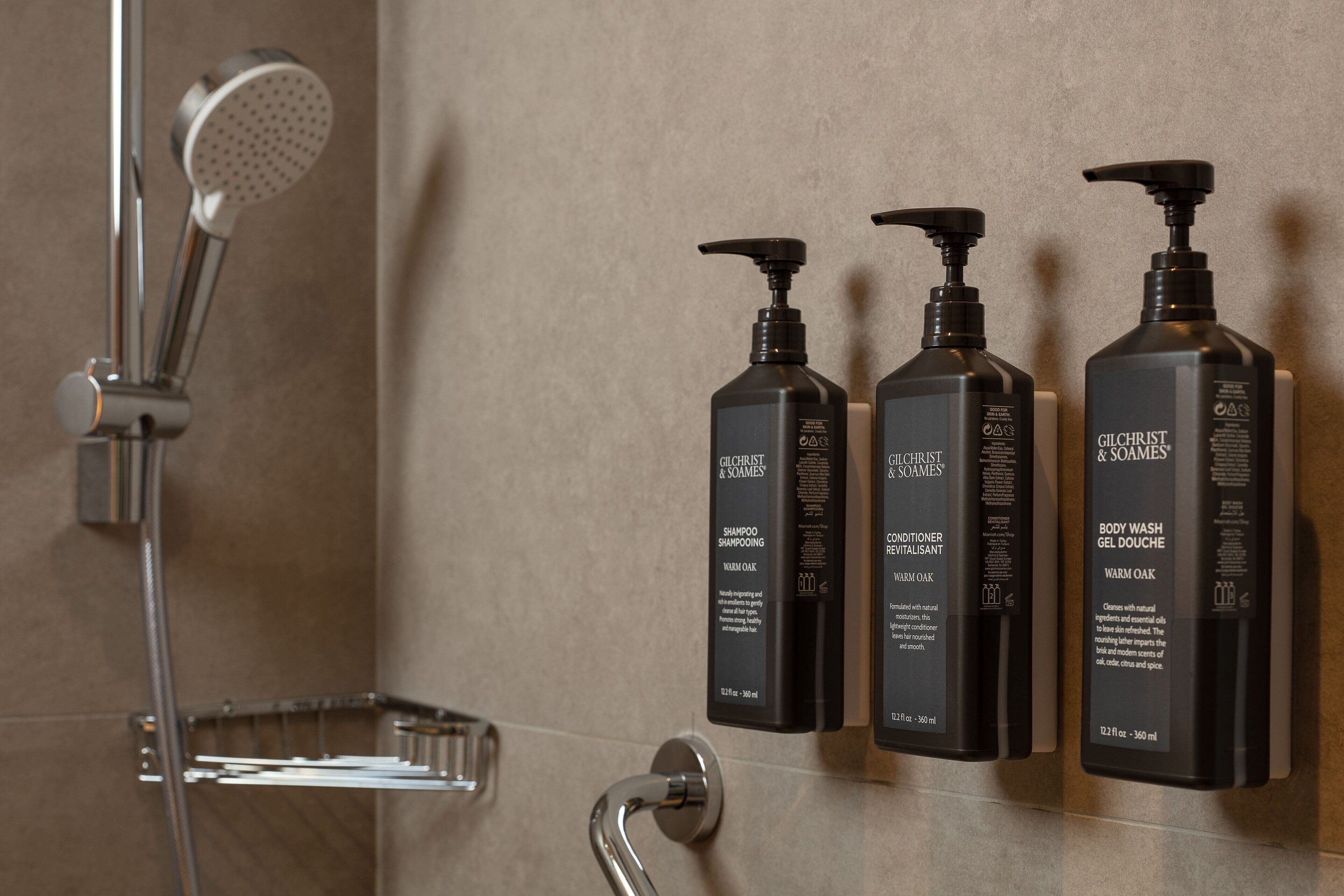 Baño con ducha, secador de manos y tres botellas de gel de baño Gilchrist & Soames.