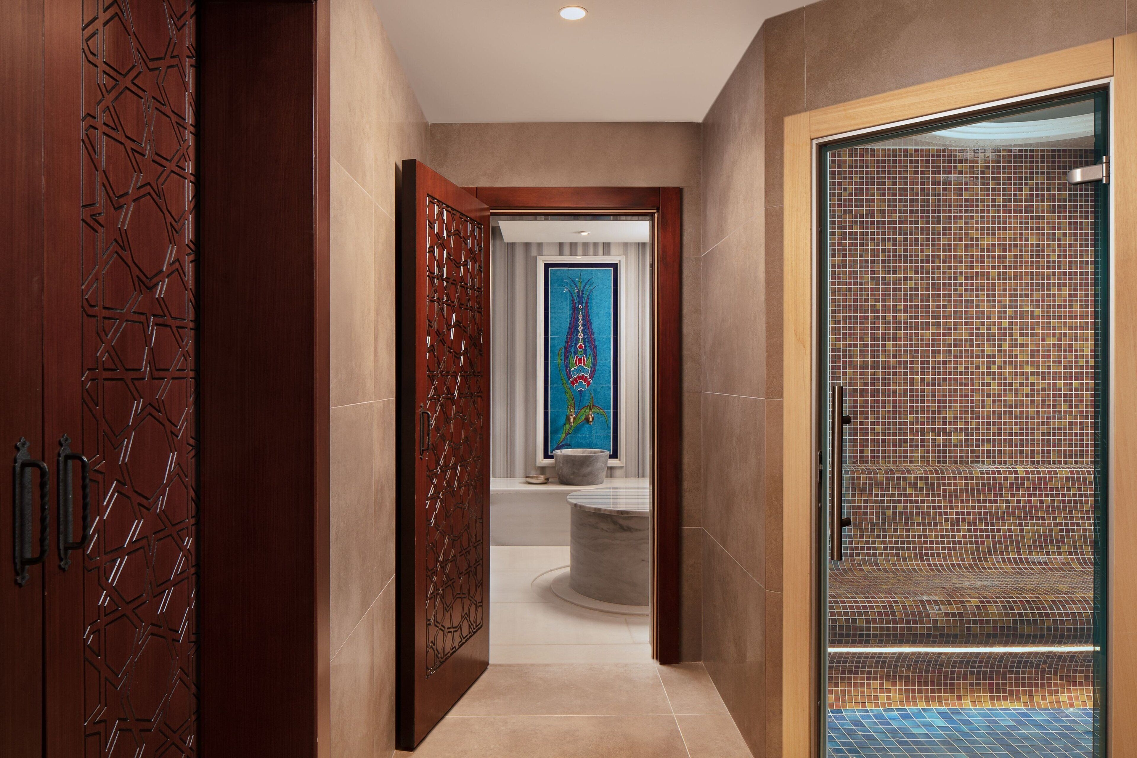 A hallway with a wooden door, a glass door leading to a bathroom, and a tiled floor.