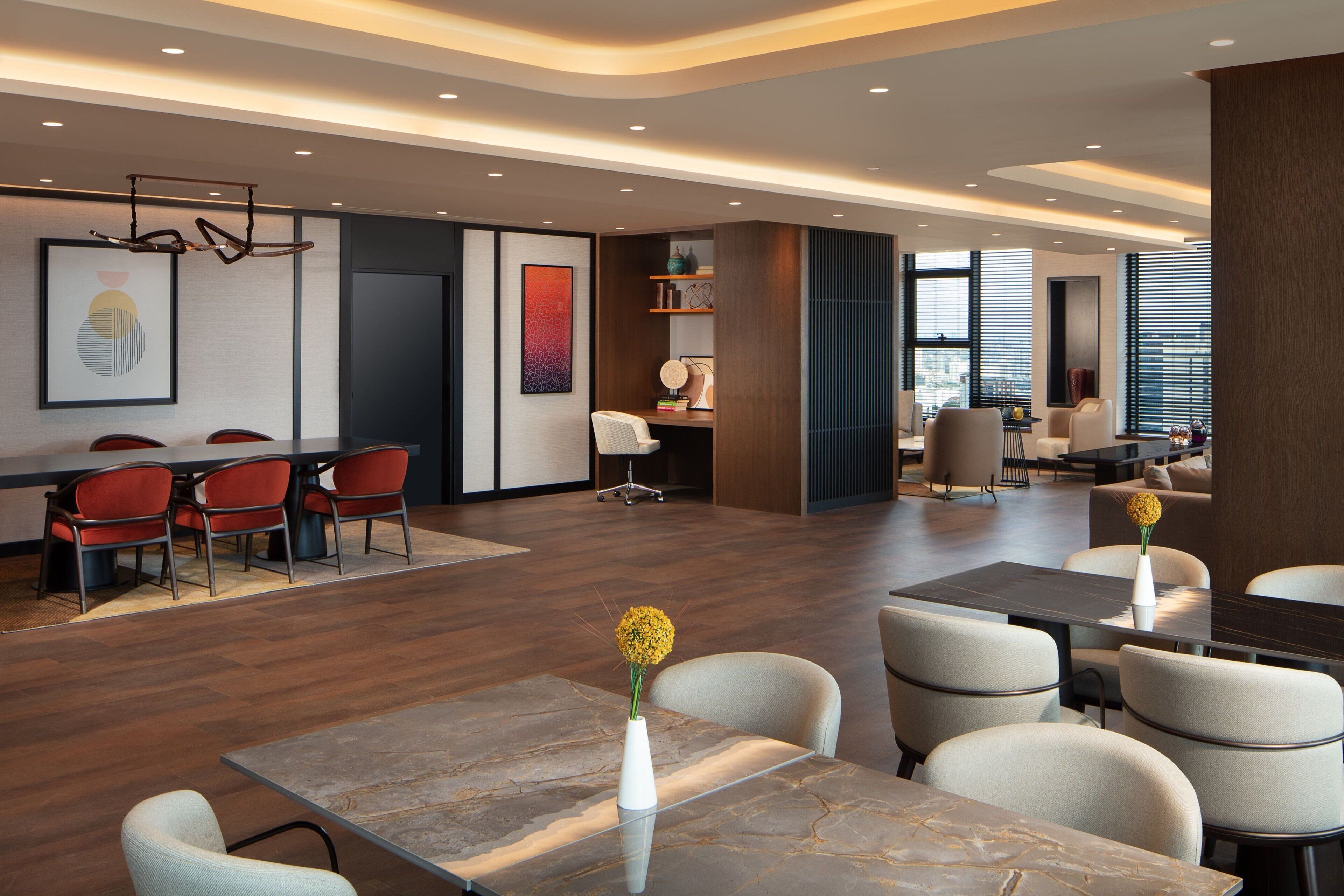 A modern hotel lobby with a long reception desk, multiple seating areas, and a large window providing natural light.
