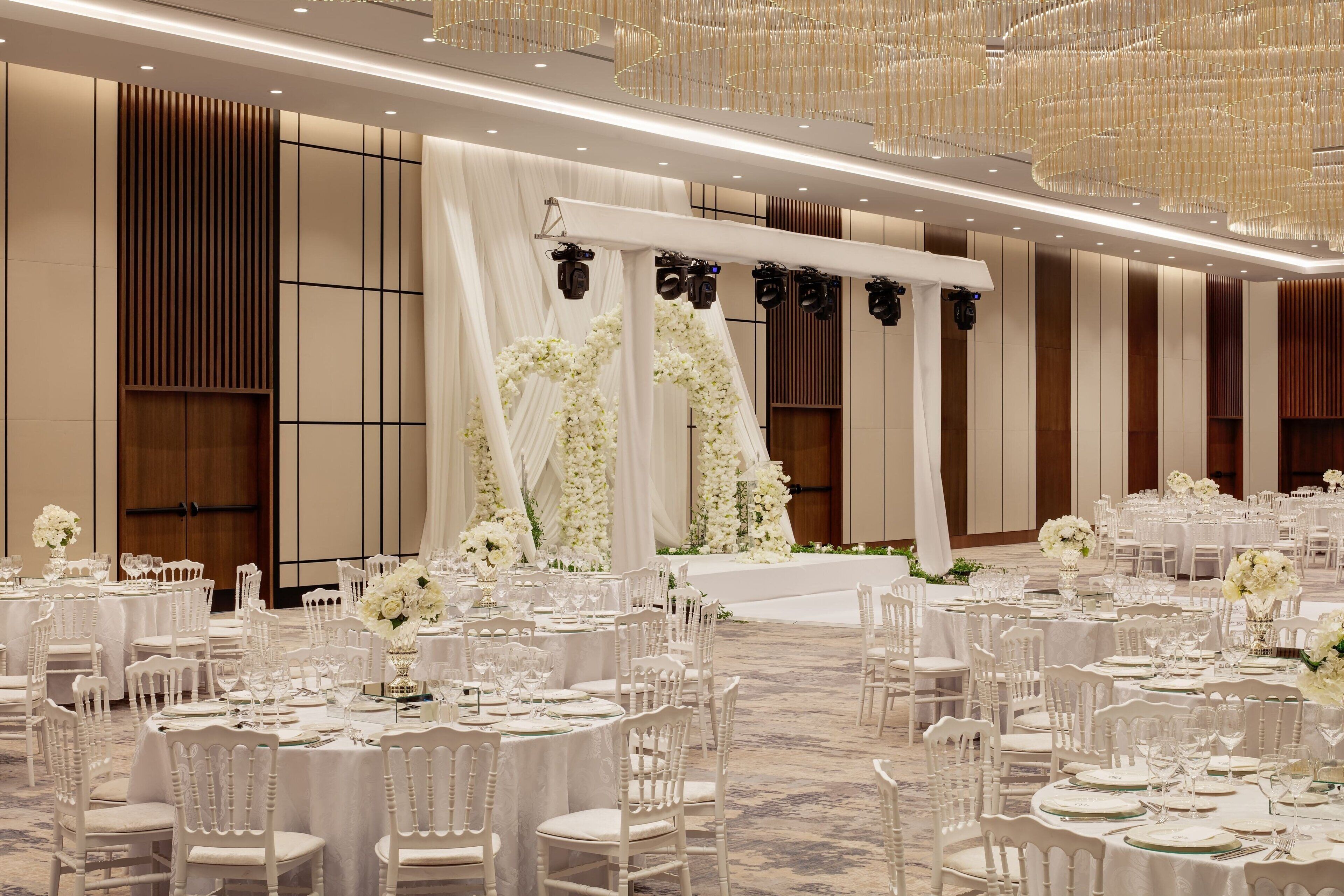 A banquet hall with round tables, white chairs, and floral centerpieces.
