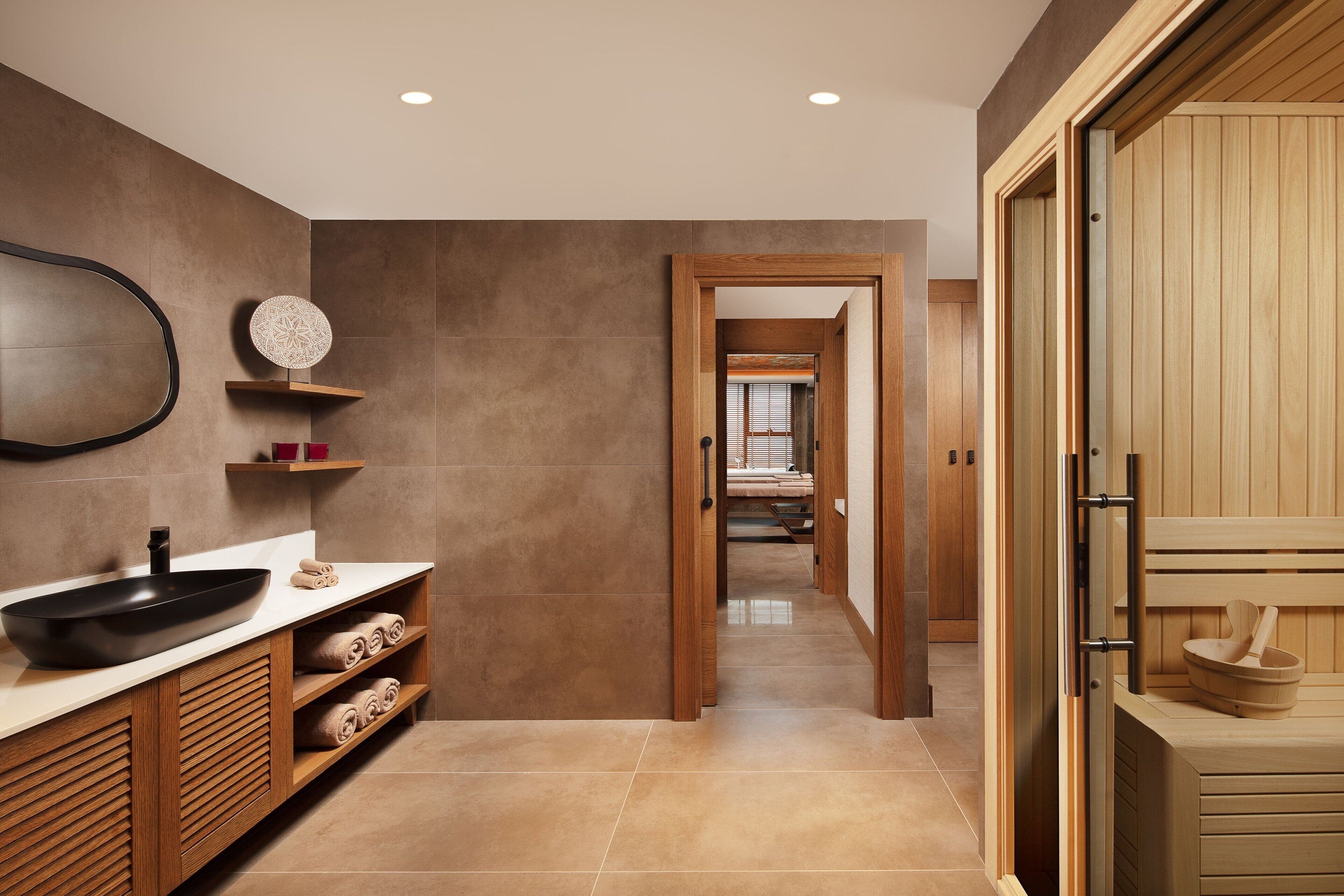 Un baño moderno con un lavamanos negro grande, armarios de madera y una zona de sauna de madera.