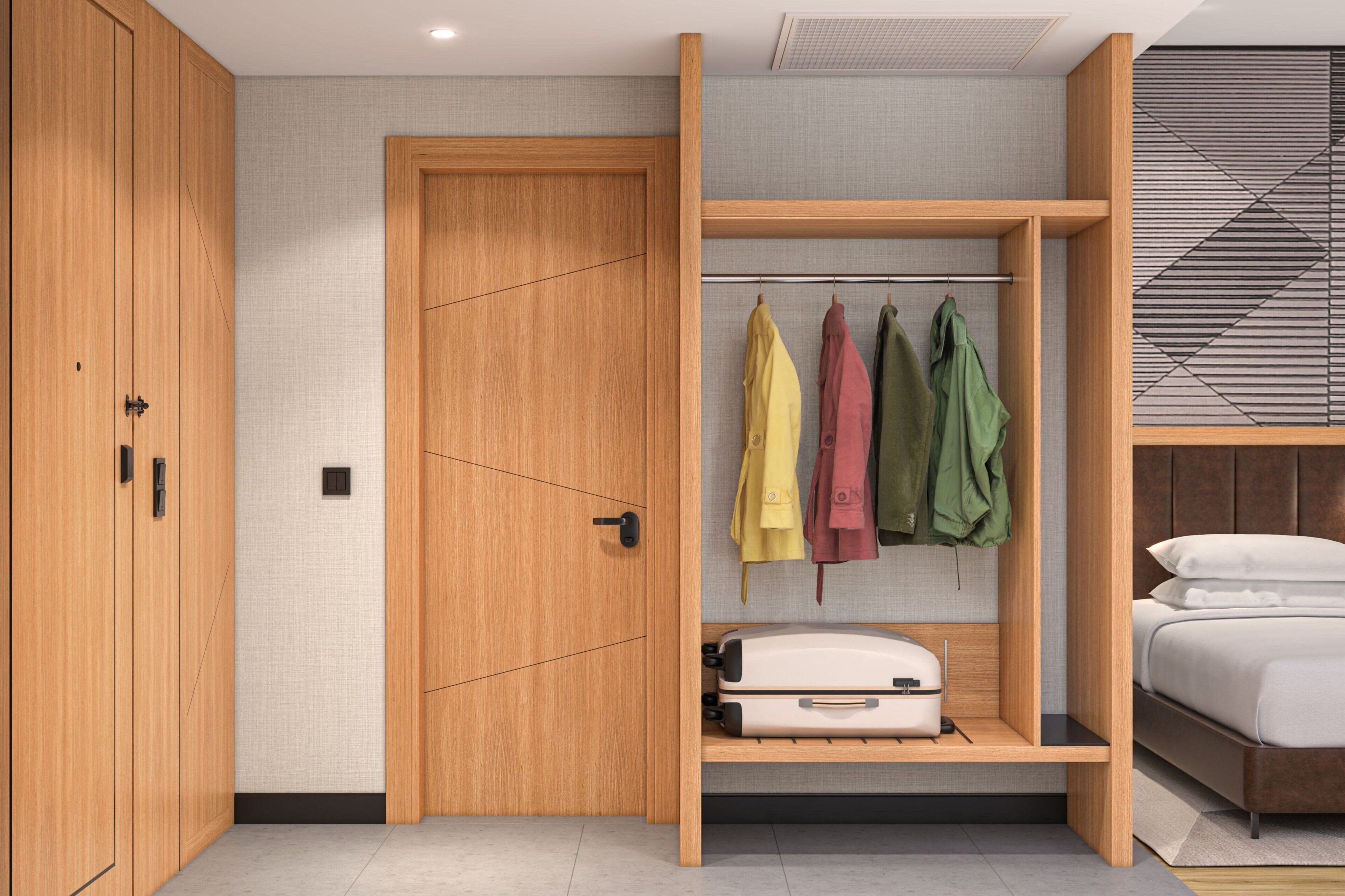 Een slaapkamer met een bed, een houten garderobe, een kapstok met jassen en een koffer op een plank.