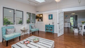 A spacious living area with a high ceiling, skylight, and a ceiling fan. There are two patterned sofas, a coffee table, and a teal cabinet with glass doors. - Outdoor Oasis - Secluded Pool, Hot Tub, Fireplace (Cary)