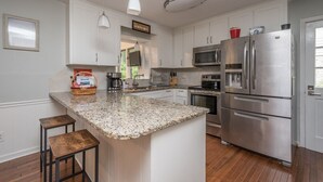 A kitchen with white cabinets, a granite countertop, stainless steel appliances, and a small island with stools. - Outdoor Oasis - Secluded Pool, Hot Tub, Fireplace (Cary)