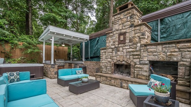 An outdoor patio with stone walls, a stone fireplace, and blue cushioned seating. - Outdoor Oasis - Secluded Pool, Hot Tub, Fireplace (Cary)