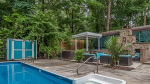 A swimming pool with a hot tub, outdoor seating, and a covered patio area surrounded by trees. - Outdoor Oasis - Secluded Pool, Hot Tub, Fireplace (Cary)