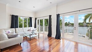 A spacious living room with a white sofa, a glass coffee table, and large windows with black curtains.