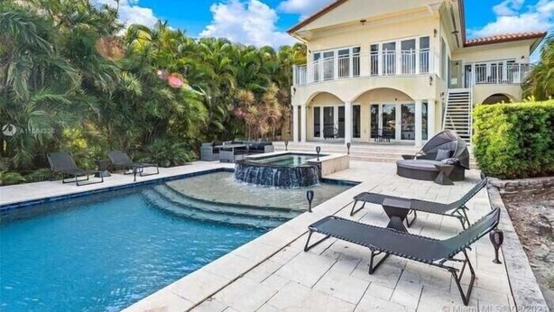 A two-story house with a swimming pool, outdoor seating, and a waterfall feature.