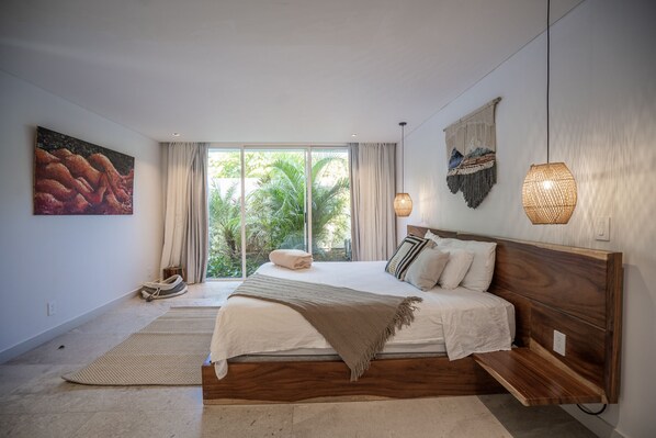 Un dormitorio moderno con una cama grande, vistas al verdor exterior y una lámpara fijada a la pared.
