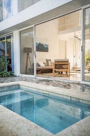 Un área de piscina moderna al aire libre con un porche acristalado, una banca de madera y un cuadro grande en la pared.