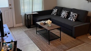 Una sala de estar con un sofá de color oscuro, una mesa de centro, un televisor y un ventilador de techo.