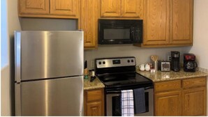 Una cocina con armarios de madera, un refrigerador de acero inoxidable, un microondas negro, una estufa y una cafetera.