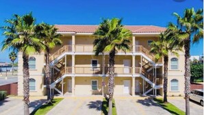 Un edificio de varios pisos con balcones, palmeras y un cielo azul despejado.
