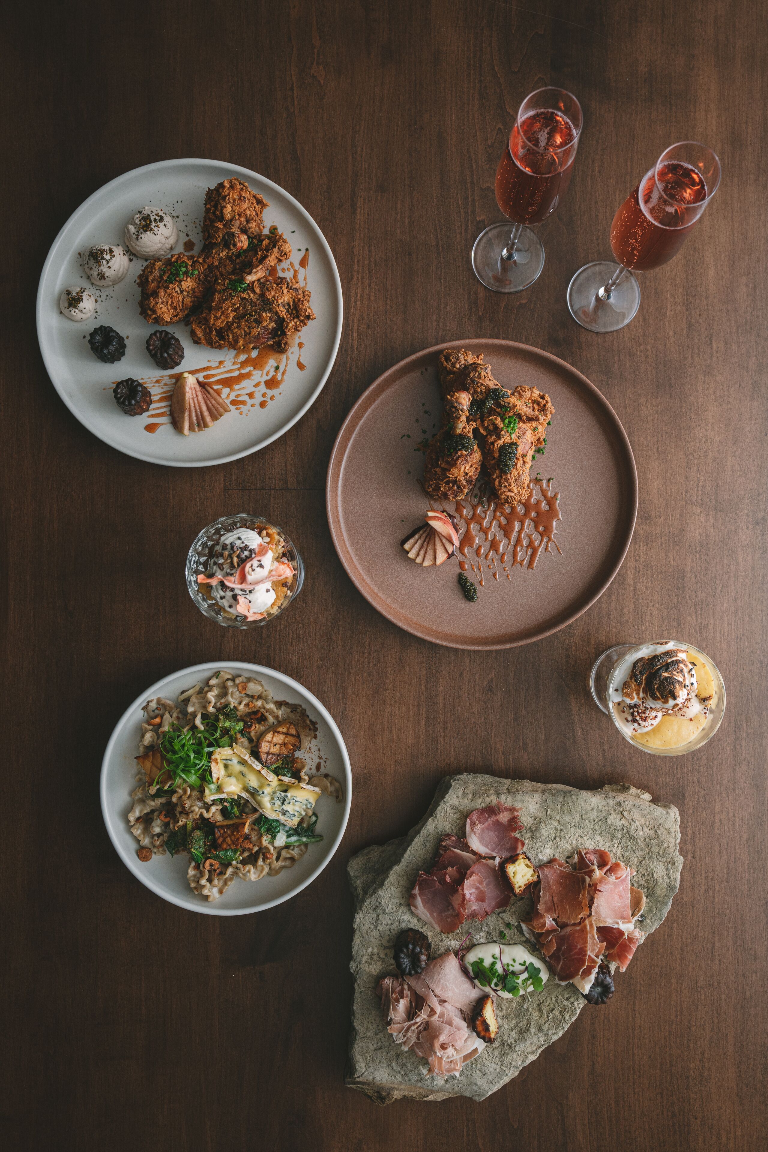 A top-down view of a dining table with various dishes, including a plate of meat, a bowl of pasta, and two glasses of a red beverage.