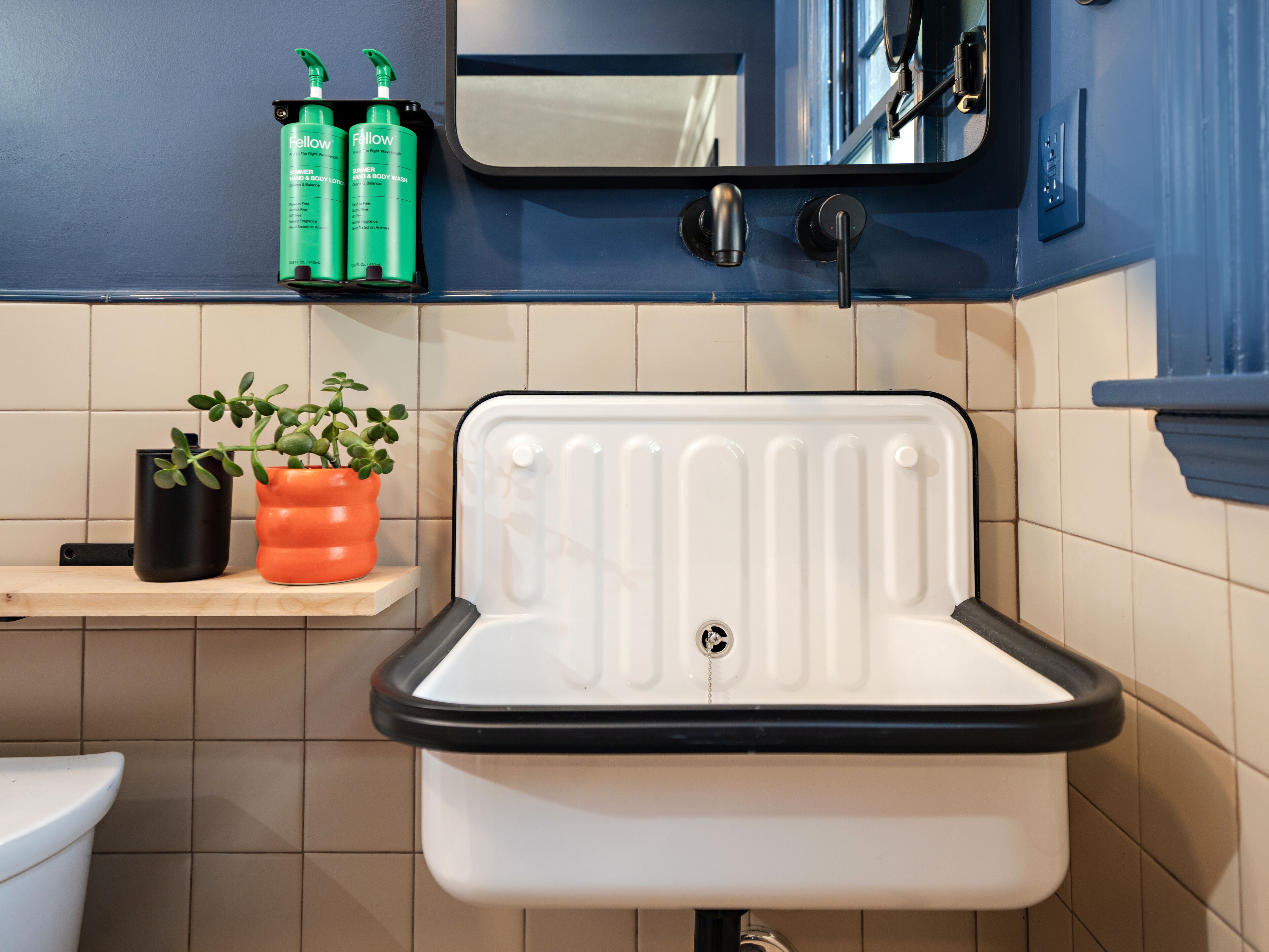 A bathroom with a white sink, a mirror above it, and a shelf with toiletries.