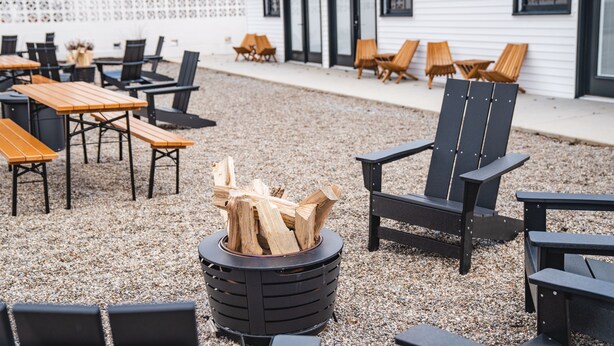 An outdoor seating area with tables and chairs, a fire pit, and a building in the background. - Bardstown Motor Lodge (Bardstown)