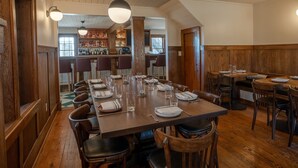 A restaurant with a long wooden table set for a meal, wooden walls, and a bar area in the background. - Bardstown Motor Lodge (Bardstown)