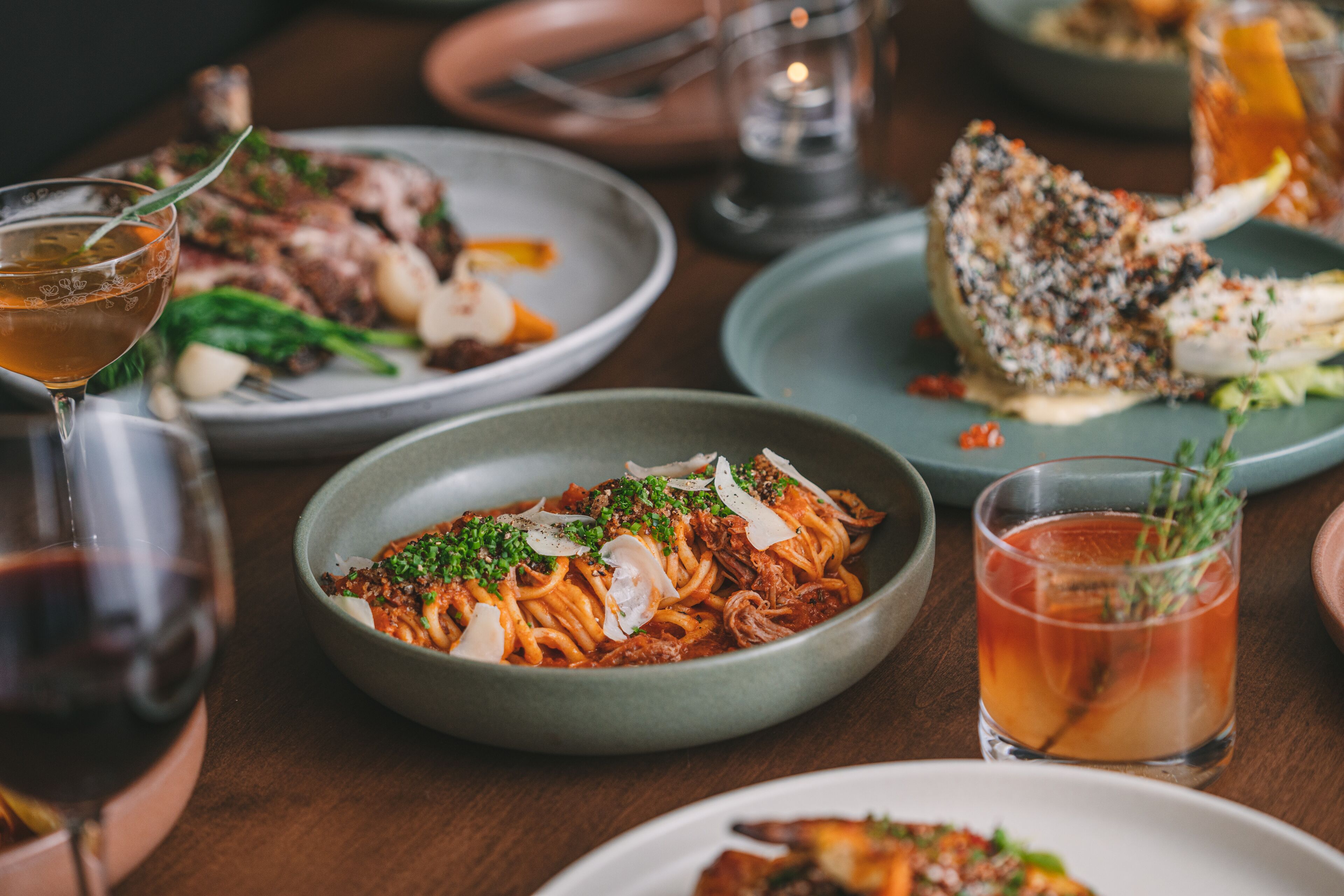 A dining table with plates of spaghetti, a glass of red wine, and a glass of iced tea.