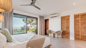A bedroom with a large bed, a ceiling fan, and a view of the outdoors. - Deluxe Modern 3 bedroom villa with pool, panoramic ocean view-5 min to the beach (Nosara)