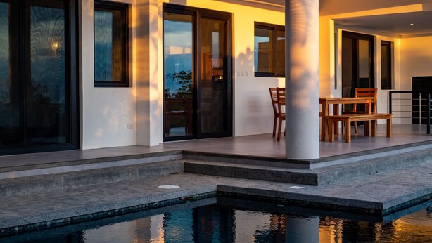 A modern outdoor pool area with a dining setup, large windows, and a view of the landscape. - Deluxe Modern 3 bedroom villa with pool, panoramic ocean view-5 min to the beach (Nosara)