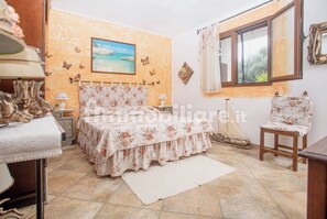 A bedroom with a bed, a chair, a window, and a painting on the wall.